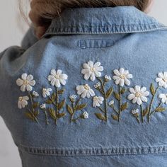 the back of a woman's jean jacket with white flowers embroidered on it and green leaves