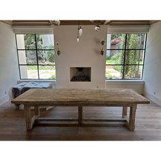 a large wooden table sitting inside of a living room next to two windows and a fire place