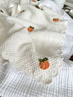 a pile of white knitted blankets with pumpkins on them sitting on top of a table