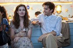 two people sitting on a blue couch with drinks in their hands and one person holding a wine glass