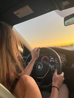 a woman driving a car with the sun setting in the background