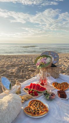 a picnic on the beach with watermelon, pizza and other foods laid out