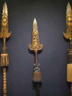 three different types of knives on display in a museum setting with blue walls and gold trimmings