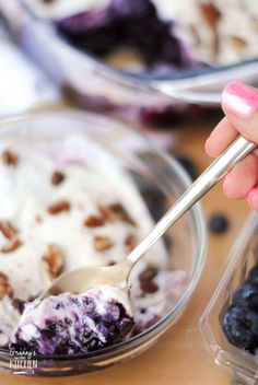 a hand holding a spoon over a bowl of blueberries and ice cream