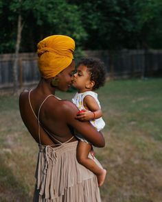 a woman holding a baby in her arms and wearing a yellow turban on top of her head