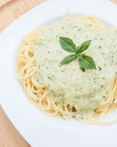 a white plate topped with pasta covered in sauce and garnished with green leaves