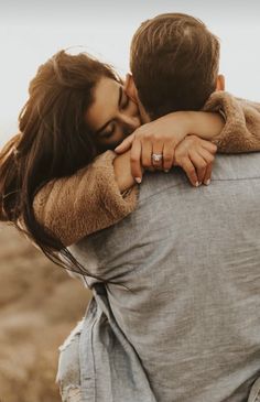 a man and woman embracing each other in the middle of an open field with brown grass