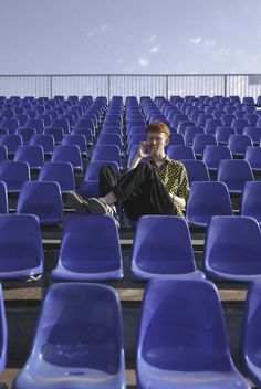 a woman sitting in the middle of rows of blue chairs with her feet on her chin