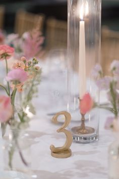 the table is set with candles and flowers in glass vases, which have numbers on them