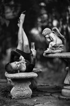 a man laying on top of a bench next to an angel statue holding a wine glass