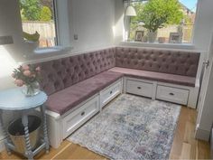 a corner bench with storage drawers in a living room next to a table and window