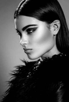 black and white photo of a woman with long hair wearing a feathered coat, looking at the camera