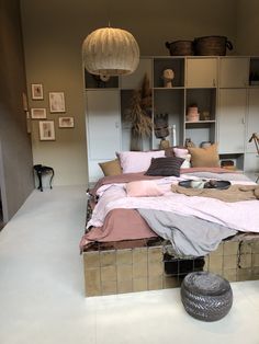 a bed with pink sheets and pillows in a room next to shelves filled with pictures