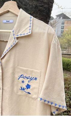 a white shirt with blue embroidery on it and a tree in the back ground behind it