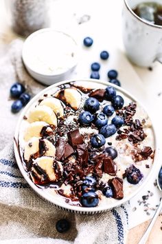 a bowl filled with cereal and blueberries on top of a table next to a cup of coffee