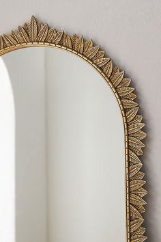 an ornate gold mirror hanging on the wall next to a white vase and potted plant