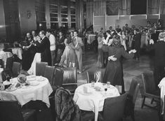 a black and white photo of people dancing at a party in a large room filled with tables