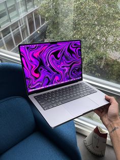 a person holding up a laptop computer in front of a window with a purple swirl design on the screen