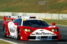 a red and white race car driving on a track with grass in the back ground