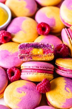colorful macaroons with raspberries and yellow sauce on them are displayed in front of other macaroons