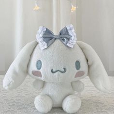 a white stuffed animal with a bow on its head sitting on a table in front of a curtain