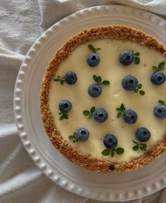 a cheesecake topped with blueberries and green leaves is on a white platter