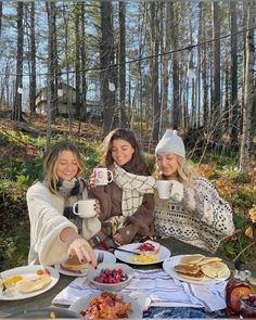 three women sitting at a picnic table with food and drinks in front of them,