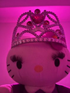 a hello kitty doll with a tiara on it's head and purple lights in the background