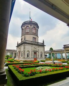 a large building with many plants and flowers in the foreground, on a cloudy day