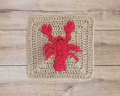 a crocheted square with a red crab on it sitting on a wooden floor