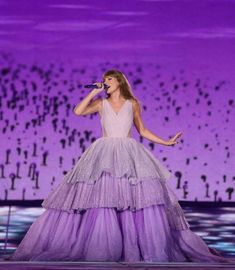 the singer is wearing a purple gown and holding a microphone in her hand as she sings on stage