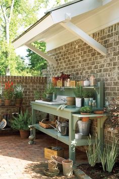 an outdoor kitchen with potted plants and pots on the stove top in front of a brick wall