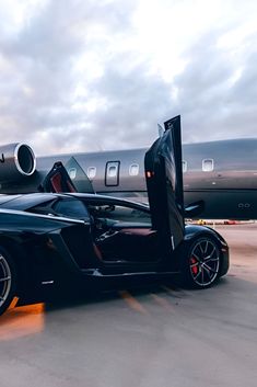 a black sports car with its door open on the tarmac next to an airplane