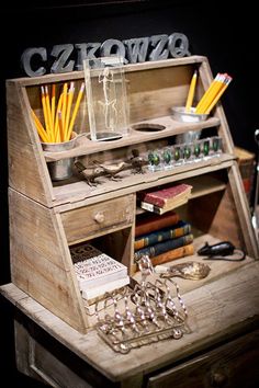 a wooden desk topped with lots of books and pencils next to a glass vase