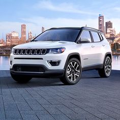 a white jeep is parked in front of a lake and the cityscape behind it