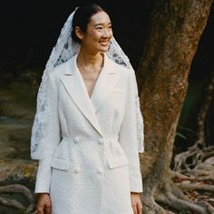 a woman wearing a white suit and veil standing next to a tree