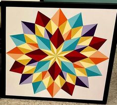 a colorful art piece is displayed on the floor in front of a wall with a black frame