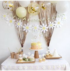 a table with cake, cupcakes and balloons in the shape of daisies