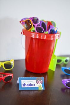 a bucket full of sunglasses sitting on top of a table next to a sign that says shades