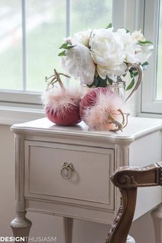 two vases with flowers and feathers on a small table in front of a window