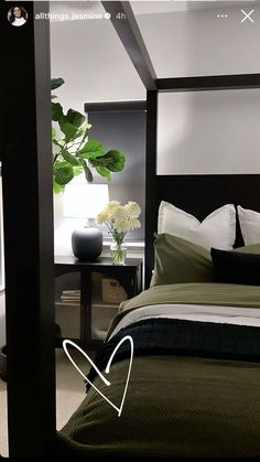 a bed with green sheets and pillows in a bedroom next to a vase filled with white flowers