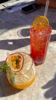 two cocktails sitting on top of a table with orange slices and garnishes