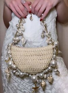 a woman in a white dress holding a purse with pearls and seashells on it