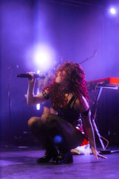 a woman with red hair is holding a microphone and kneeling on the floor in front of a stage