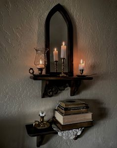 a shelf with candles and books on it in front of a mirror that is hanging from the wall