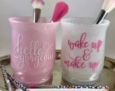 two pink and white makeup brushes on a silver tray next to a cup with the words wake up make up