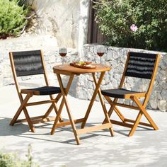 two chairs and a table with food on it in front of a stone wall outside