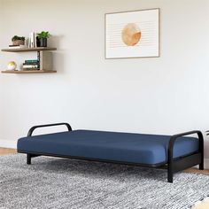 a blue day bed sitting on top of a rug next to a wall mounted book shelf