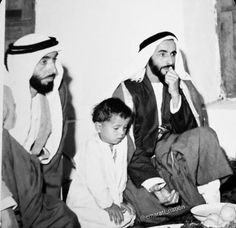 an old black and white photo of three men sitting on the floor with food in front of them