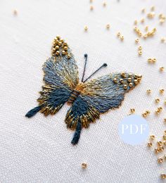 a close up of a butterfly made out of beads on a white cloth with gold beading